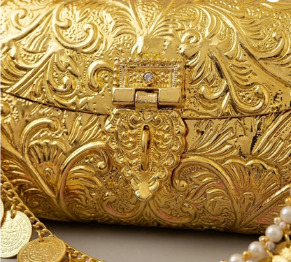 Close-up of a gold-plated clutch purse showing carved floral engravings and decorative hanging gold coins