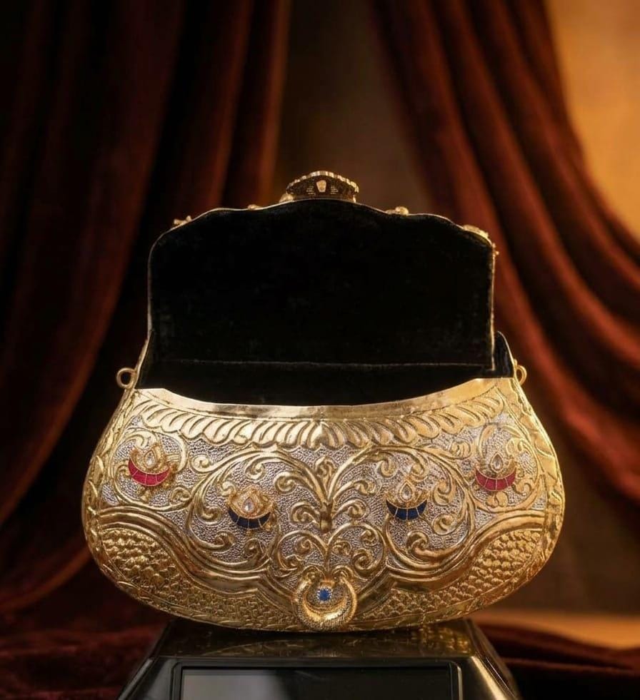 Royal antique gold metal clutch with an ornate floral embossed design, multicolour stone embellishments and a circular top handle for weddings and festive occasions.